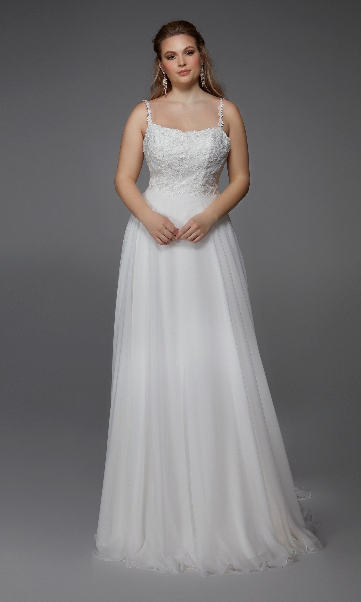 A woman models the Alyce 7018 long dress in diamond white, featuring a chiffon A-line skirt, lace bodice detailing, and thin straps, standing against a plain gray background.